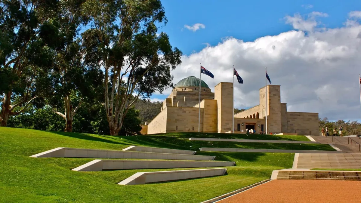 The Australian War Memorial with its green dome, flags and terraced lawns under a blue sky.