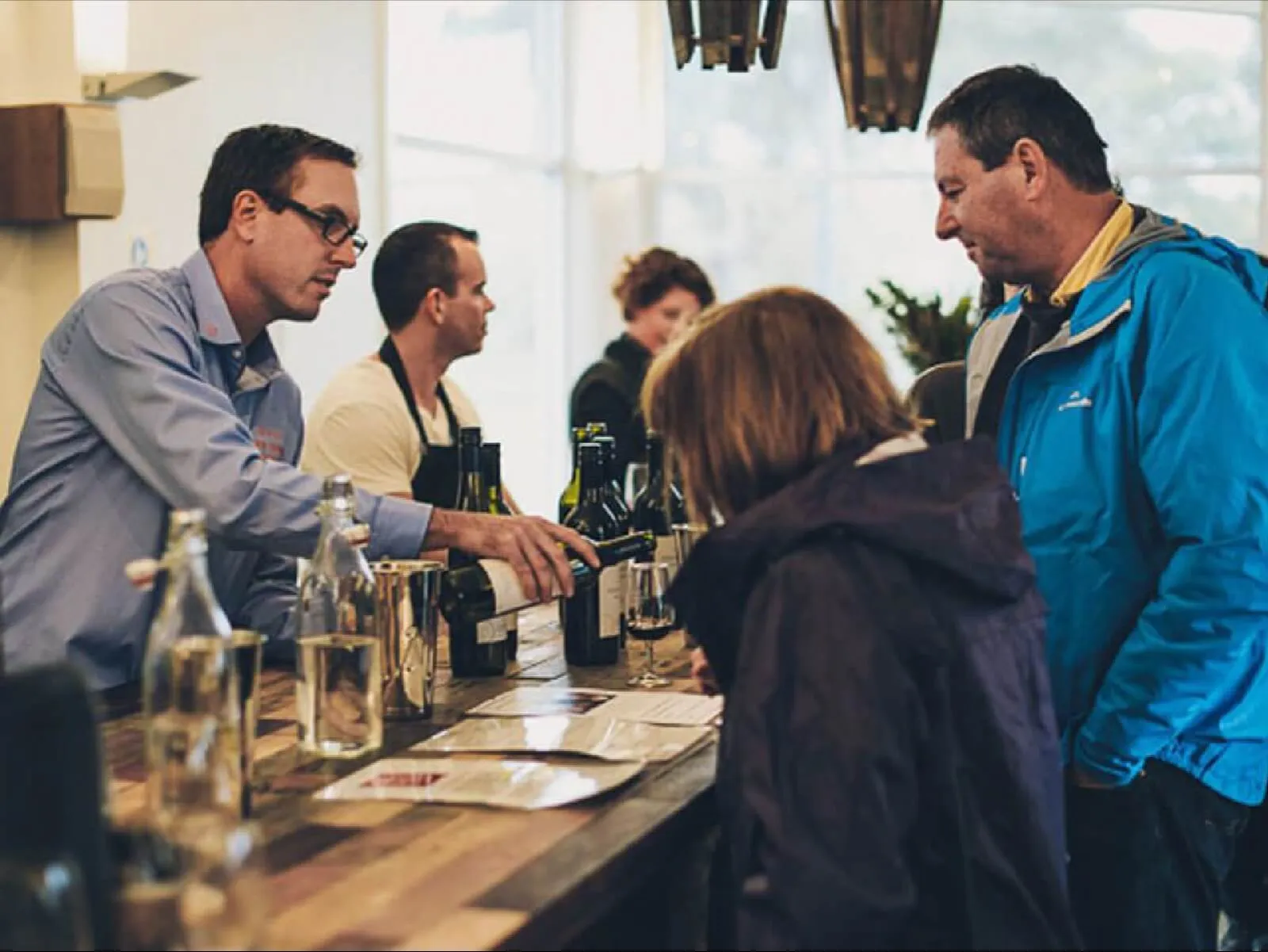 A winemaker pours tastings for a group of guests at a cellar door counter.