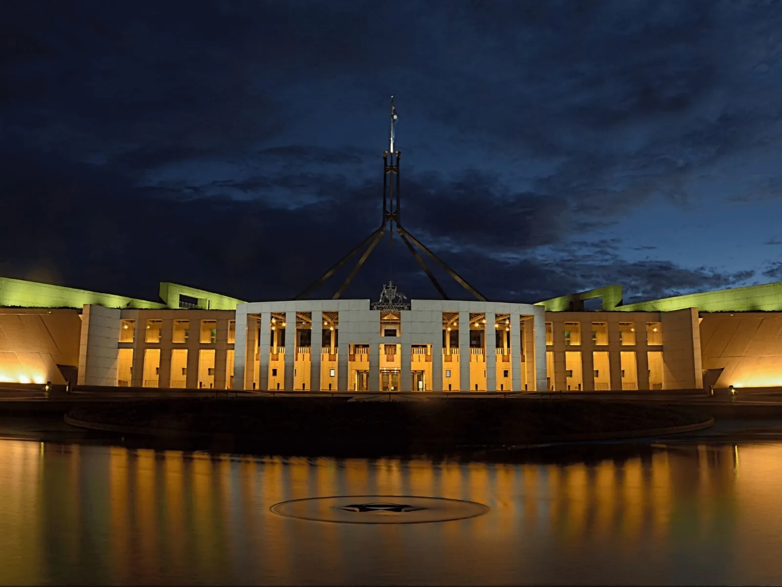 Parliament House lit up at night and reflected in the forecourt pool.