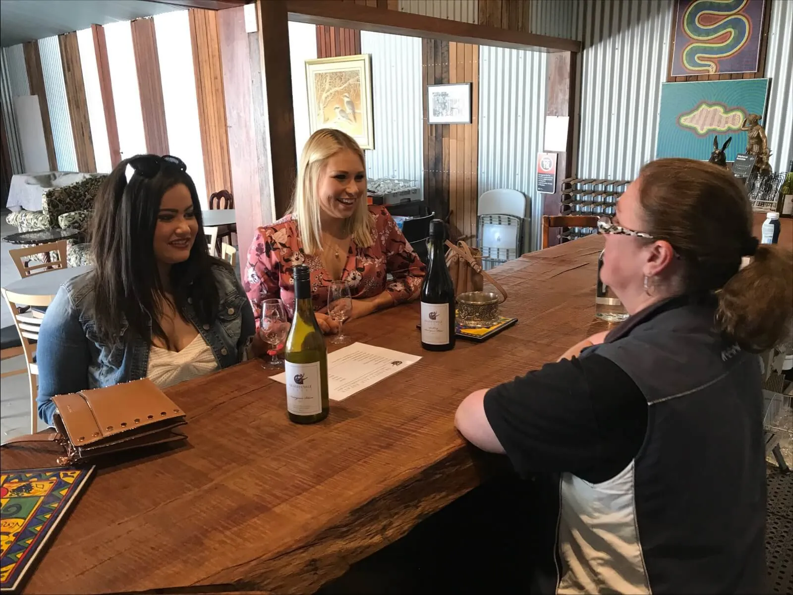 Three women taste wine at a timber cellar door bar.