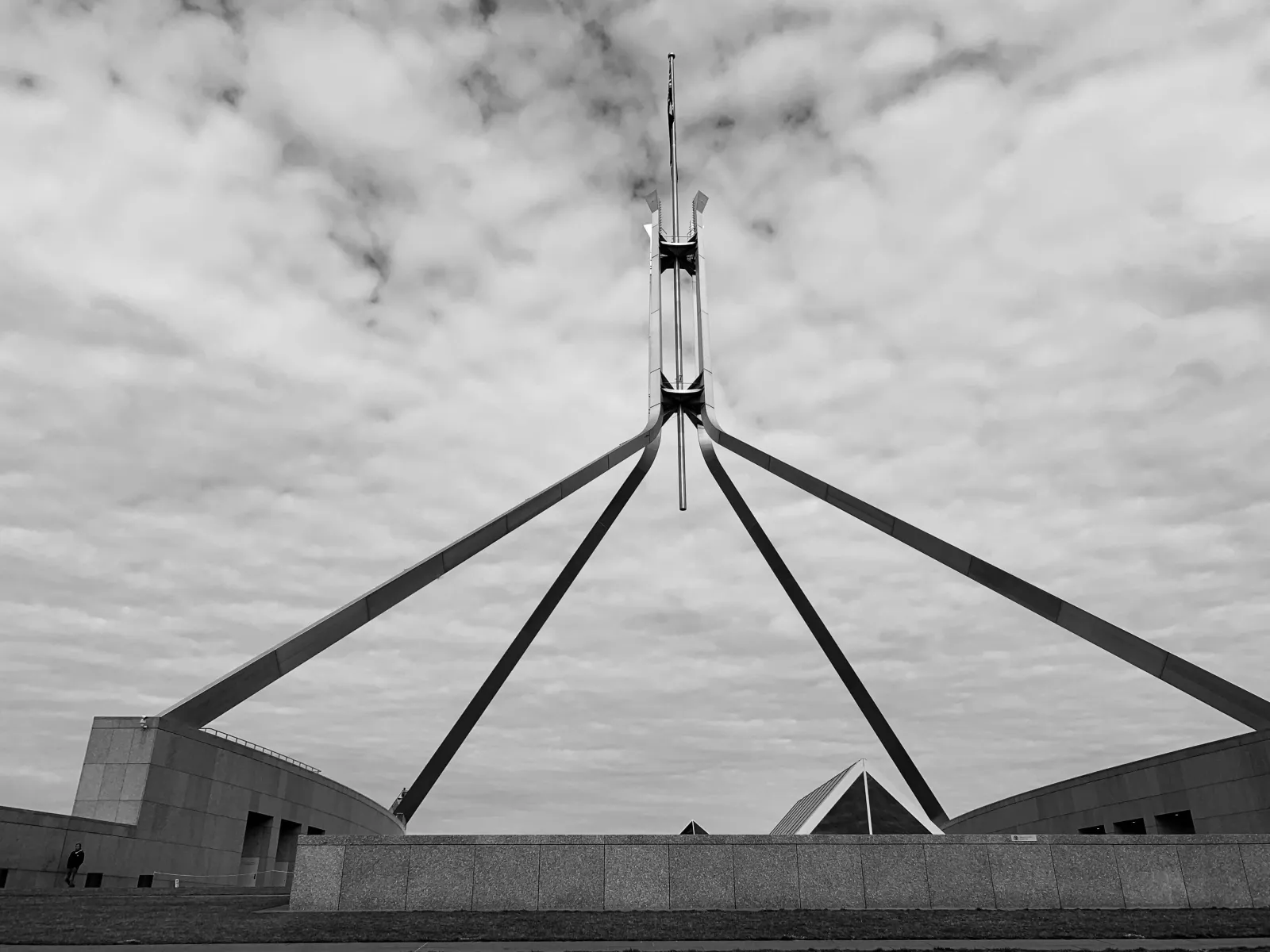 The Parliament House flagpole against a cloudy sky, in black and white.