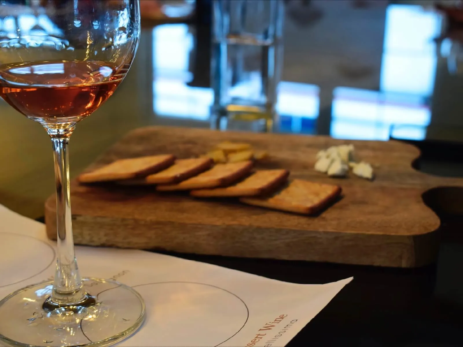 A glass of rosé beside a board of crackers and cheese.