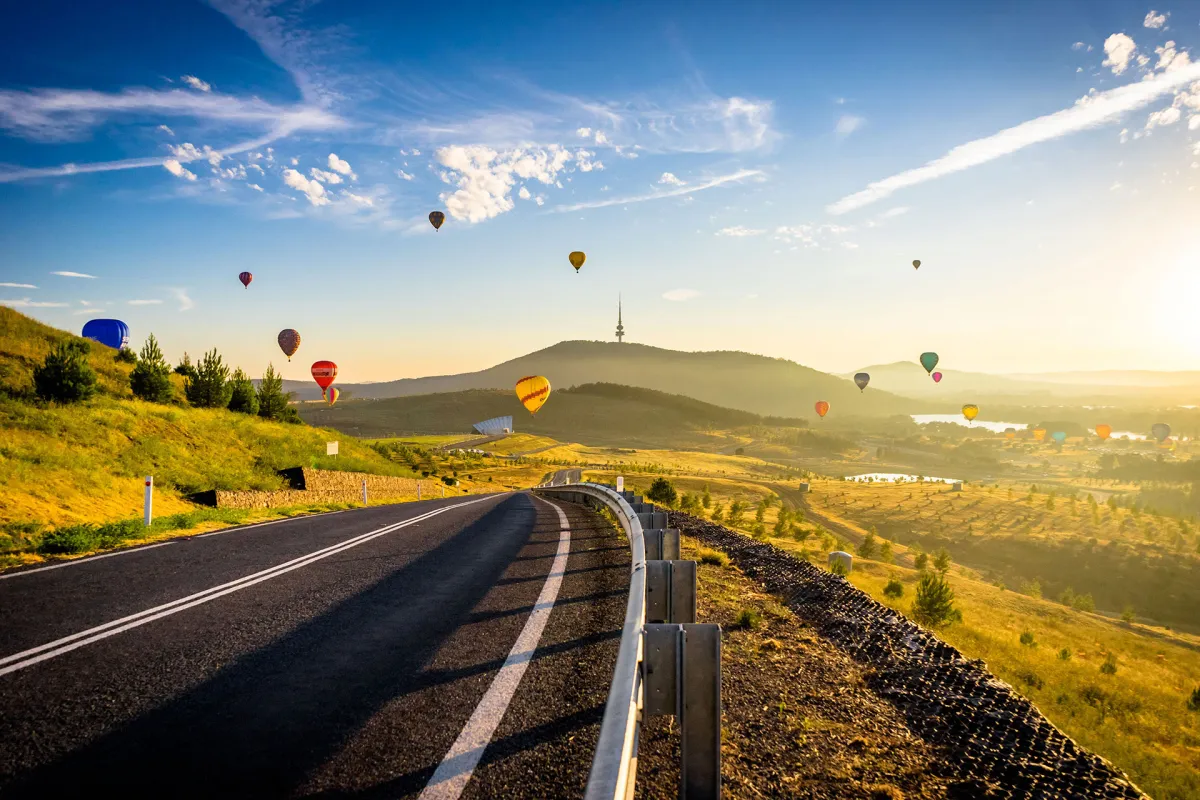 Hot air balloons over a winding road near Canberra at sunrise, with Telstra Tower on Black Mountain in the distance