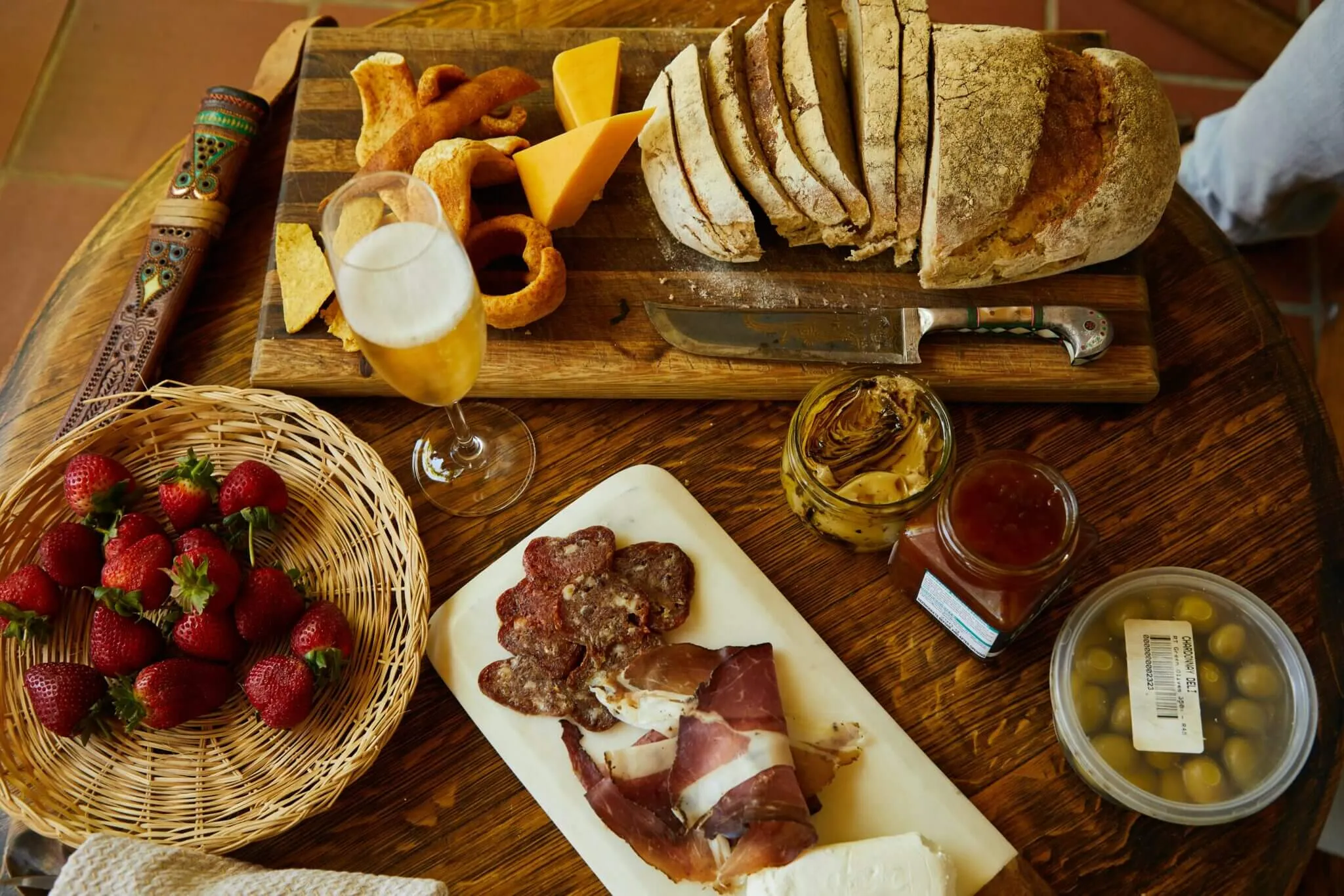 A board of bread, cheese, strawberries and cured meats with a glass of beer on a wooden table.
