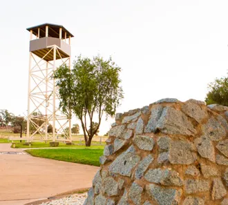 A tall timber guard tower beside a stone wall at the Cowra prisoner of war camp site.