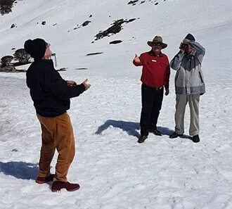 A guide in a red shirt and hat with two visitors on a snowy slope.