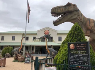 Entrance to the National Dinosaur Museum with a large Tyrannosaurus rex sculpture looming over the courtyard.