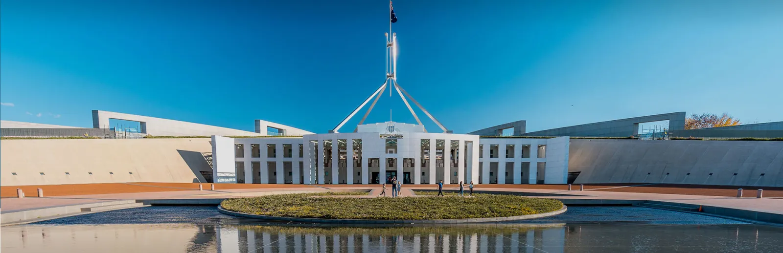 Parliament House, Canberra, with its flag mast above the forecourt pool under a clear blue sky