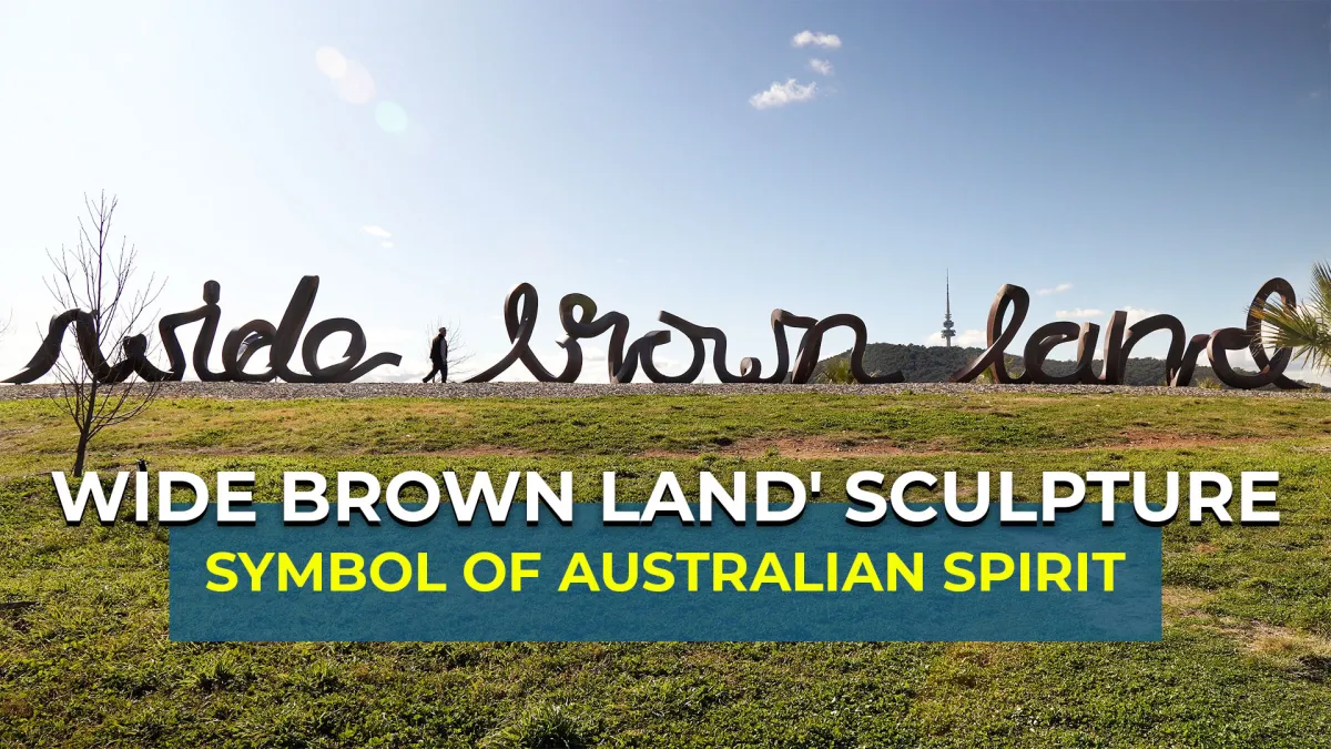 Large cursive metal sculpture spelling Wide Brown Land stretches along a grassy ridge with a lone pedestrian walking nearby and a distant communications tower under a clear blue sky, while a bold two-line foreground banner proclaims WIDE BROWN LAND SCULPTURE and SYMBOL OF AUSTRALIAN SPIRIT.