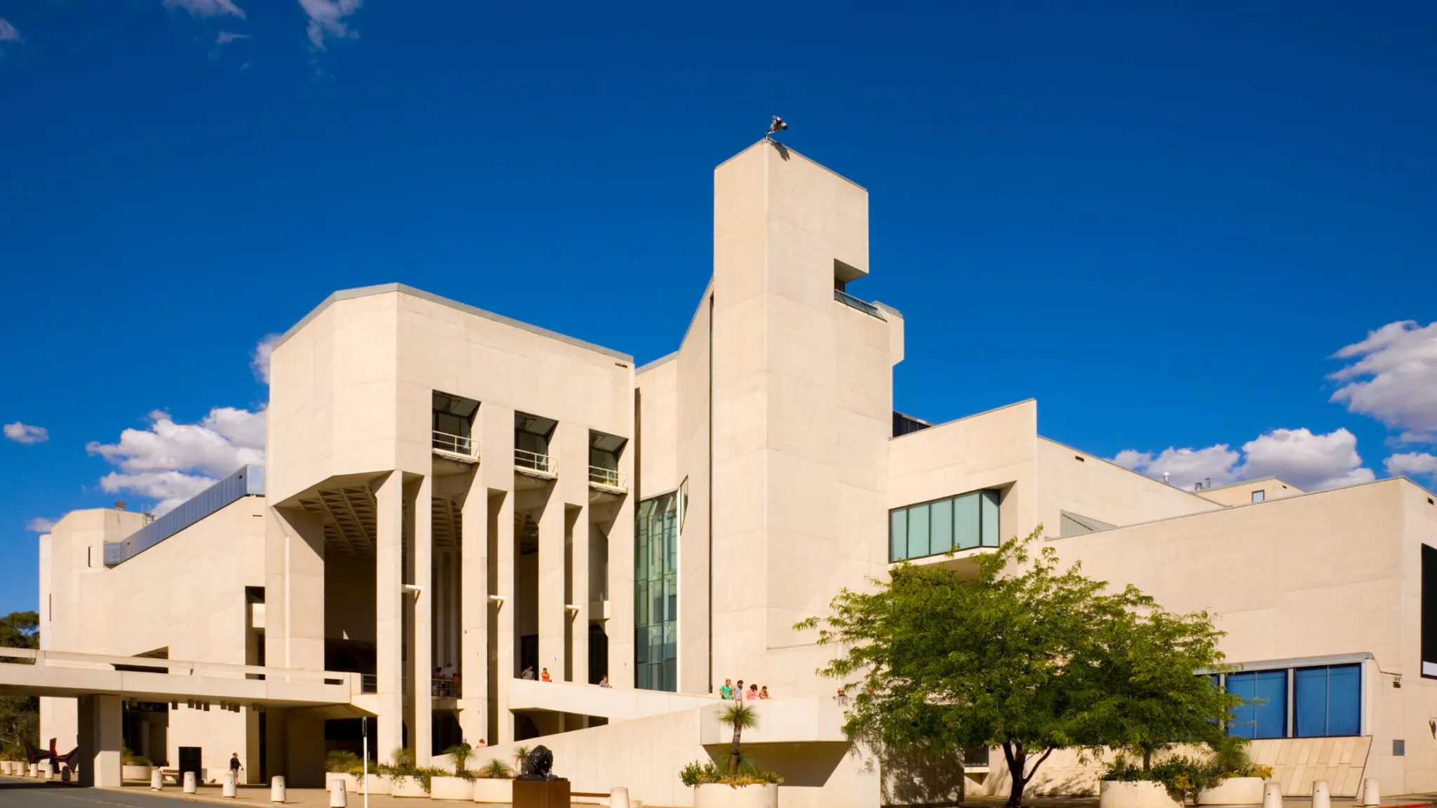 The National Gallery of Australia, a modern white concrete building with tall glass windows, under a deep blue sky.