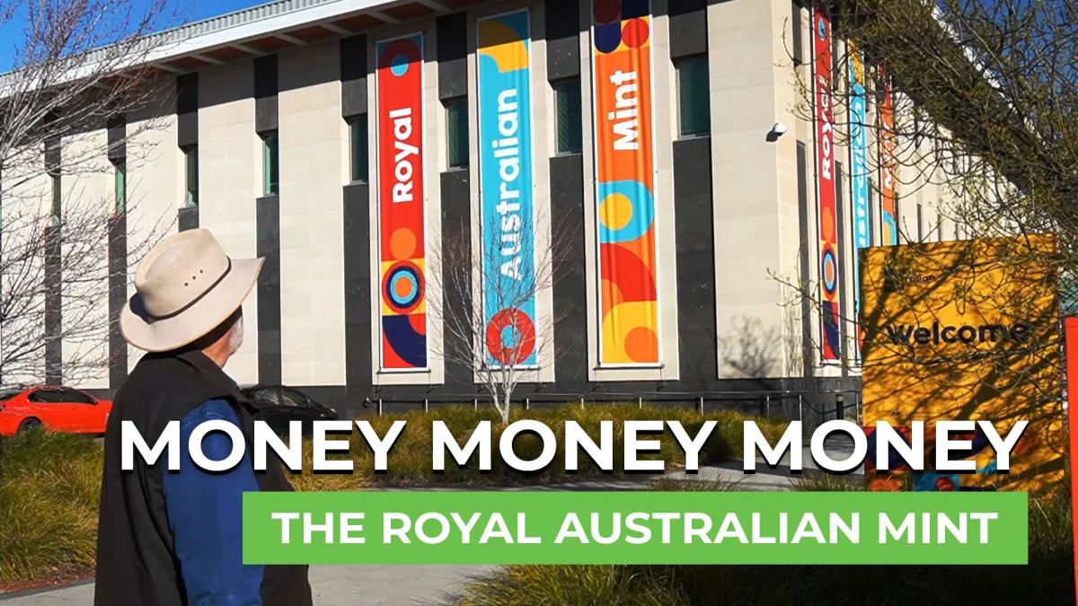 A man wearing a beige hat and dark jacket stands outdoors looking at the Royal Australian Mint building, which displays tall colorful vertical banners reading 'Royal', 'Australian' and 'Mint' with large overlaid text 'MONEY MONEY MONEY' and 'THE ROYAL AUSTRALIAN MINT'.