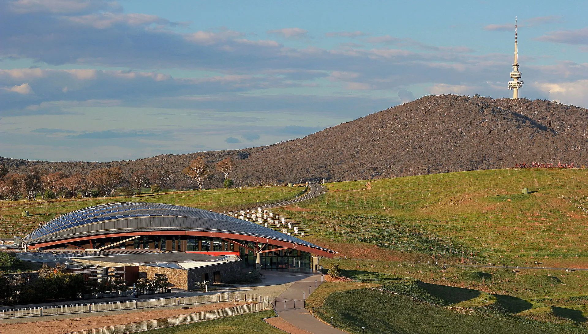 The National Arboretum visitor centre with its curved roof, with Black Mountain and Telstra Tower behind.