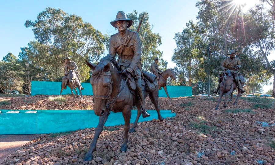 Bronze statues of mounted soldiers on a rocky slope in front of the turquoise wall of the Boer War Memorial.