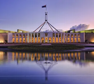 Parliament House lit up at dusk and reflected in the forecourt pool.